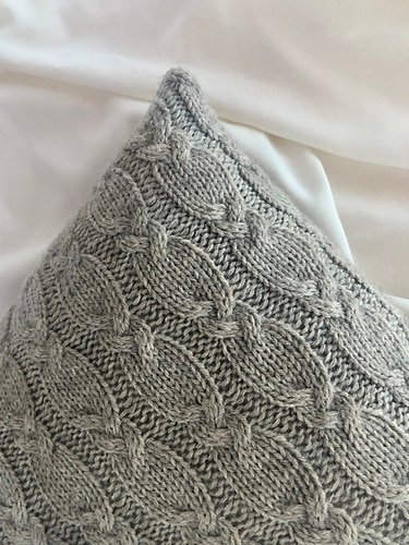 a grey handknitted pillow with all over cables