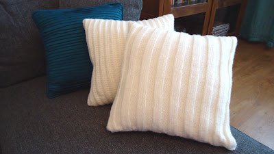 three pillows on a couch, one is dark blue and two are white and handknitted