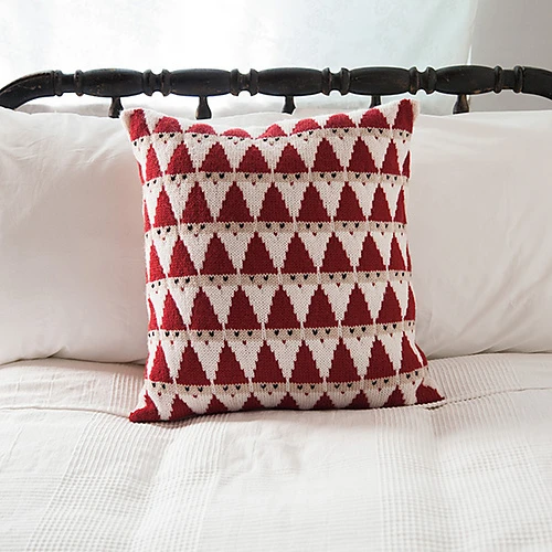 a handknitted pillow with a geometric all over santa pattern in red and white sitting on a bed