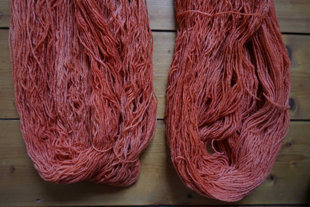 two hanks of naturally dyed, orange-red yarns on a wooden background