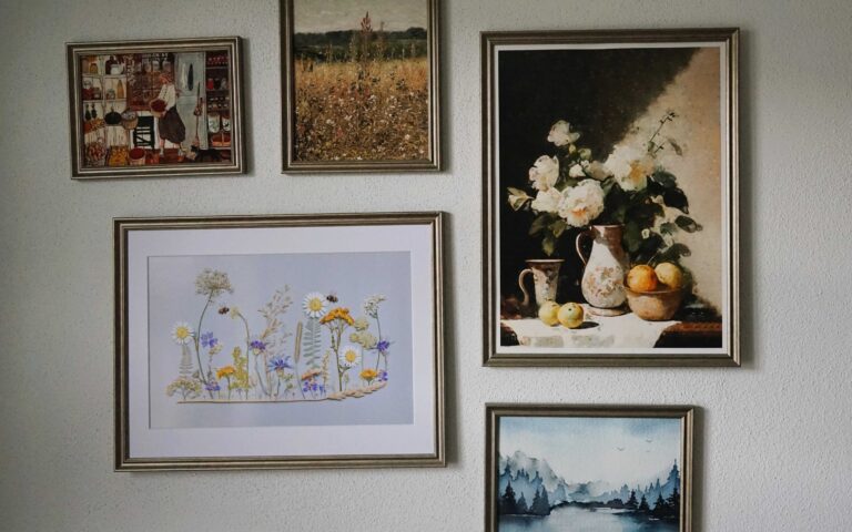 gallery wall on a white background. five pictures in silver wooden frames with prints of flowers, a still life and landscapes.