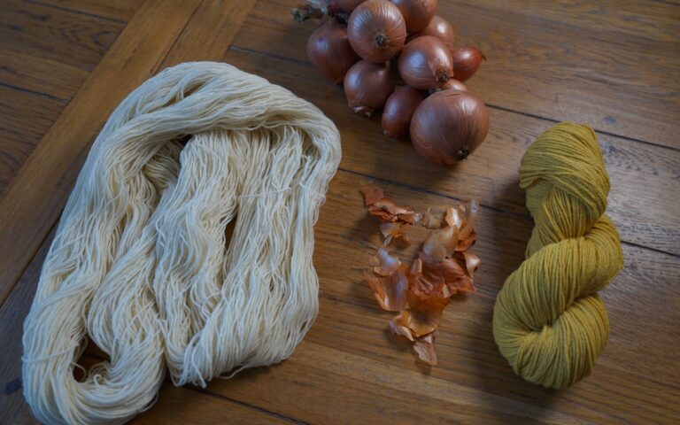 a white undyed hank of yarn and a yellow skein of yarn laying on a wooden table, next to some onions and onion skins